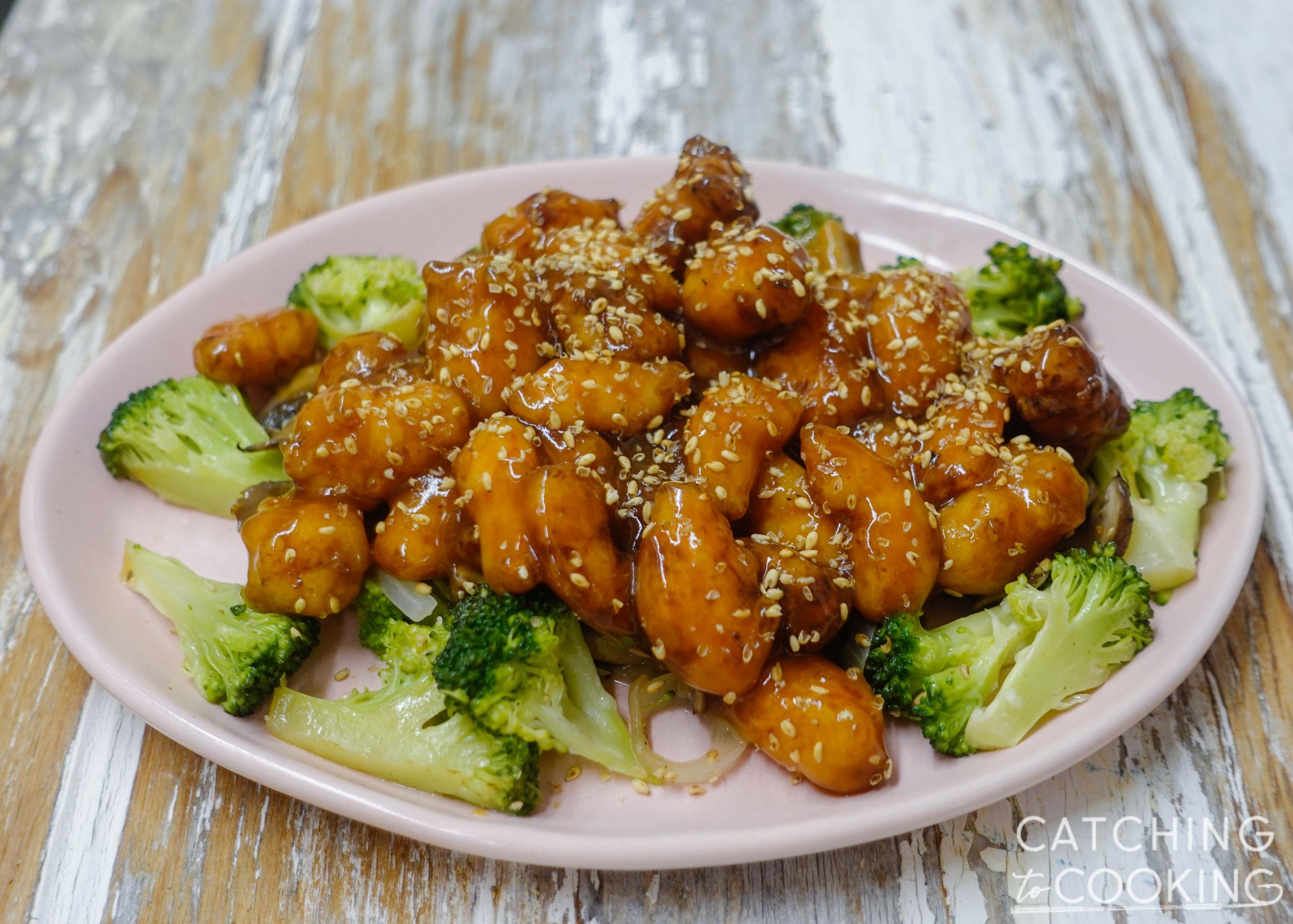 Plate of fried shrimp in sauce with sesame seeds over steamed vegetables